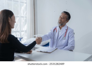 Senior doctor warmly shaking hands with a female patient in a hospital room, both smiling, showing care and trust during a consultation. A healthcare moment - Powered by Shutterstock