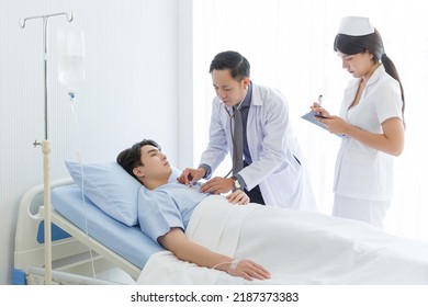 Senior doctor and young male patient who lie on the bed while checking pulse, consult and explain with nurse taking note and supporting in hospital wards. - Powered by Shutterstock