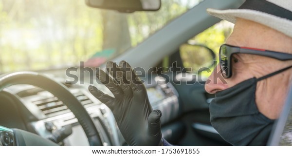 senior\
driver in black sterile gloves and mask waves hand sitting at\
steering wheel in car salon extreme close\
view
