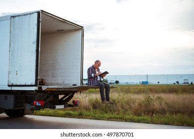 Senior driver reading a document while sitting on a truck.  