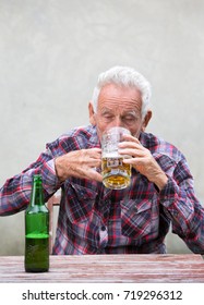 Senior Drunk Man Drinking Beer From Mug At Table