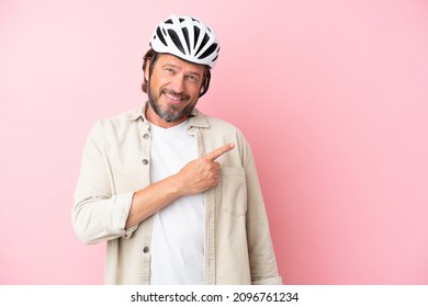Senior dutch man with bike helmet isolated on pink background pointing to the side to present a product