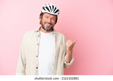 Senior dutch man with bike helmet isolated on pink background pointing to the side to present a product