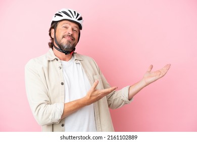 Senior dutch man with bike helmet isolated on pink background extending hands to the side for inviting to come