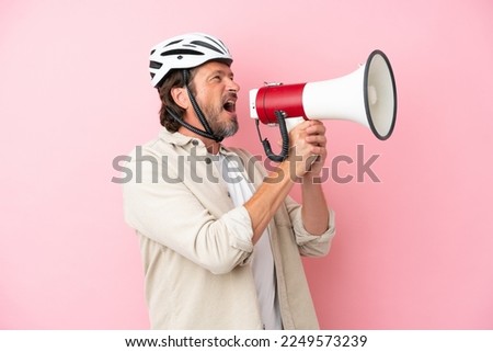 Senior dutch man with bike helmet isolated on pink background shouting through a megaphone