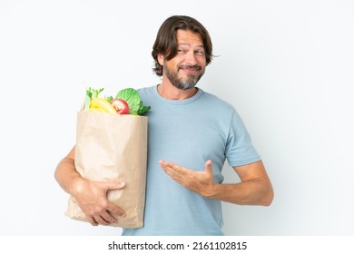 Senior dutch man holding grocery shopping bag over isolated background extending hands to the side for inviting to come