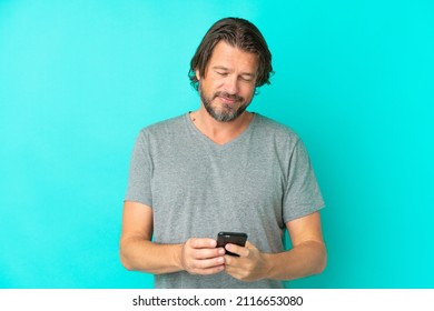 Senior dutch man isolated on blue background sending a message with the mobile