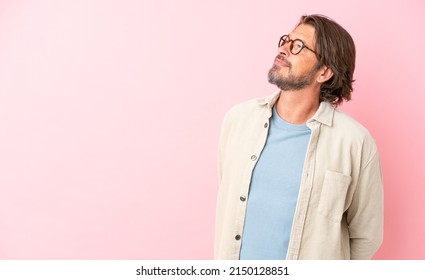 Senior dutch man isolated on pink background looking to the side and smiling