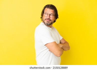 Senior dutch man isolated on yellow background looking to the side and smiling