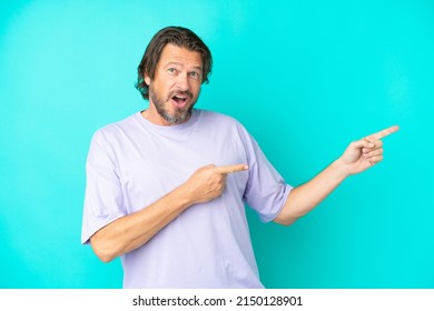 Senior dutch man isolated on blue background surprised and pointing side