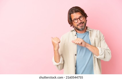 Senior dutch man isolated on pink background pointing to the side to present a product