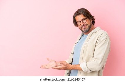 Senior dutch man isolated on pink background extending hands to the side for inviting to come