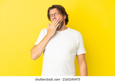 Senior dutch man isolated on yellow background yawning and covering wide open mouth with hand