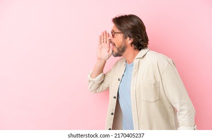 Senior dutch man isolated on pink background shouting with mouth wide open to the side