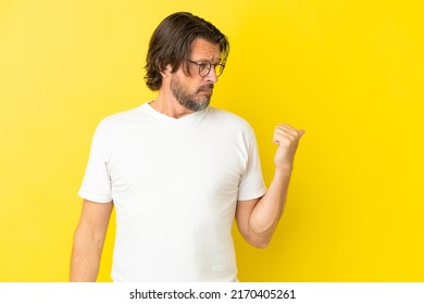 Senior dutch man isolated on yellow background unhappy and pointing to the side