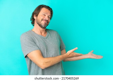 Senior dutch man isolated on blue background extending hands to the side for inviting to come
