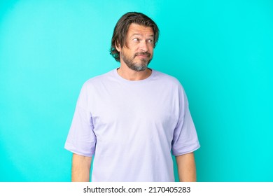 Senior dutch man isolated on blue background making doubts gesture looking side