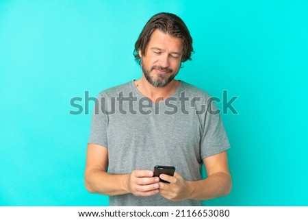 Senior dutch man isolated on blue background sending a message with the mobile