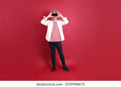 A senior East Asian man in a white shirt stands against a deep red background. - Powered by Shutterstock