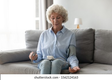 Senior Elder Woman Measure High Low Blood Pressure Test Holding Using Medical Digital Electronic Meter Sit On Sofa At Home, Heart Disease Atherosclerosis Prevention, Hypotension Hypertension Concept