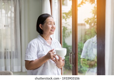 Senior elderly Asian woman drinking tea or coffee near the windows at home. Retirement, health care and ageing concept - Powered by Shutterstock