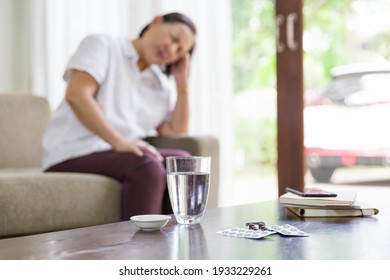 Senior Elderly Asian Woman Having A Headache While Sitting On Sofa At Home. Older Woman Is Sick, Unwell And Taking Medicine. Selective Focus