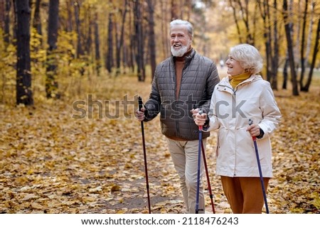senior elderly grandmother grandfather training Nordic walking with ski trekking poles in forest. Old man woman tourists hiking with sticks in forest. Active rest outdoors of mature couple