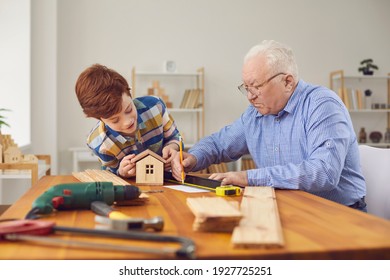 Senior Elderly Man Grandfather And His Smiling Grandson Boy Making Measures For Constructing Wooden Birdhouse At Home Together. Happy Family, Hobby, Grandfather And Child Concept