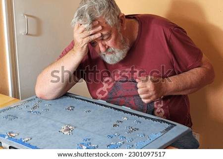 Senior or elderly man having problems trying to do a jigsaw puzzle at home. 