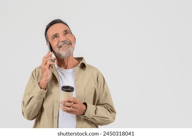 A senior, elderly man looks cheerful while talking on a phone, isolated on a white background, holding a reusable coffee cup - Powered by Shutterstock