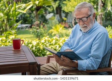 Senior elderly man reading book with mug of coffee in garden - Powered by Shutterstock