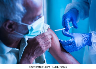 Senior Elderly Patient With Mask Getting Vaccination Or Jab At Hospital - Docotor In Protective Hazmat Suit Treating Covid Patient Injecting Anti-viral Vials At Covid Care Centre.