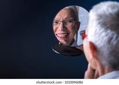 Senior Elderly Woman Applying Make Up, Looking Herself At A Hand Mirror