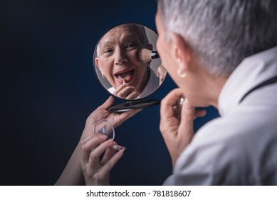 Senior Elderly Woman Applying Make Up, Looking Herself At A Hand Mirror