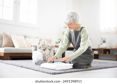 Senior (elderly) woman folding laundry towels in the living room. - Powered by Shutterstock