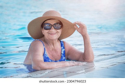 Senior (elderly) woman (over age of 50) in swimsuit, hat and sunglasses relaxing in resort swimming pool. Happy retired female  enjoying summer vacation in hotel. All inclusive. Copy space. - Powered by Shutterstock