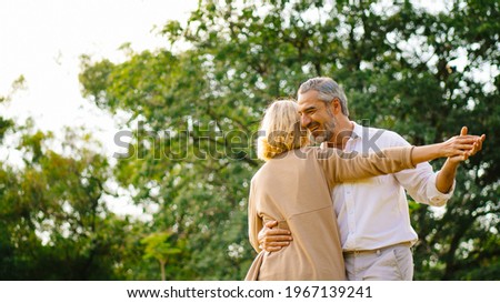 Senior elegant caucasian couple dancing looking at each other feeling love and cherish on their anniversary in the park with copy space, happily retired spouse, well-managed retirement life concept.