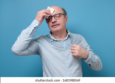 Senior Employee Sweating In A Warm Office Wiping A Forehead. Hyperhidrosis Concept. Studio Shot.