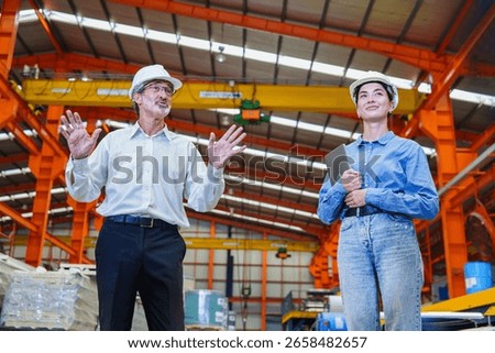 Senior engineer explaining procedures to young female staff in roofing sheet factory. Interaction shows teamwork and knowledge sharing in industrial environment.
