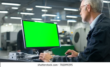 Senior Engineer In Glasses Is Working On A Desktop Computer With A Green Screen On Monitor In A Factory.
