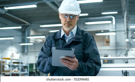 Senior Engineer In Hardhat Is Using A Tablet Computer In A Factory.