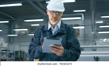 Senior Engineer In Hardhat Is Using A Tablet Computer In A Factory.