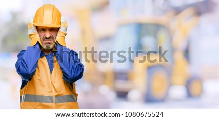 Senior engineer man, construction worker covering ears ignoring annoying loud noise, plugs ears to avoid hearing sound. Noisy music is a problem. at work