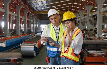 Senior engineer manager trains new employee within the metal sheet factory. Everyone wear safety vest and hardhat. Various kind of industrial machine are in the working area. - Shutterstock ID 2311557867
