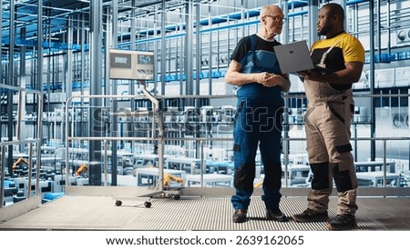 Senior engineer talking with intern in smart factory, collecting and analyzing data. Experienced technician helping trainee use tracking software in industrial plant equipped with sensors, camera A