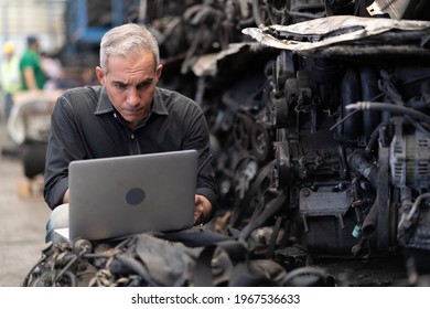 Senior Engineer Using Laptop Computer Checking List Old Used Car Engine In Machinery Parts Shop Warehouse. Old Technician Man Repair Vehicle Automobile Machine In Recycle Motor Factory