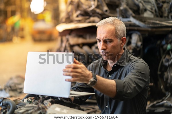 senior\
engineer using laptop computer checking list old used car engine in\
machinery parts shop warehouse. old technician man Repair vehicle\
automobile machine in Recycle motor\
factory