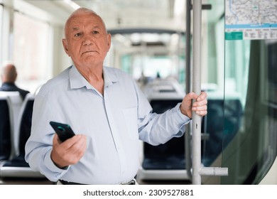 Hombre europeo de alto rango con smartphone en la mano parado dentro del tranvía y esperando su parada.