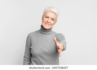 A senior European woman extends her hand in a friendly handshake against a white backdrop, highlighting the concept of s3niorlife engagement - Powered by Shutterstock