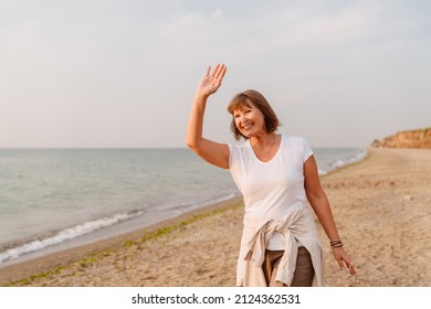 Senior european woman smiling and gesturing while walking on sandy beach